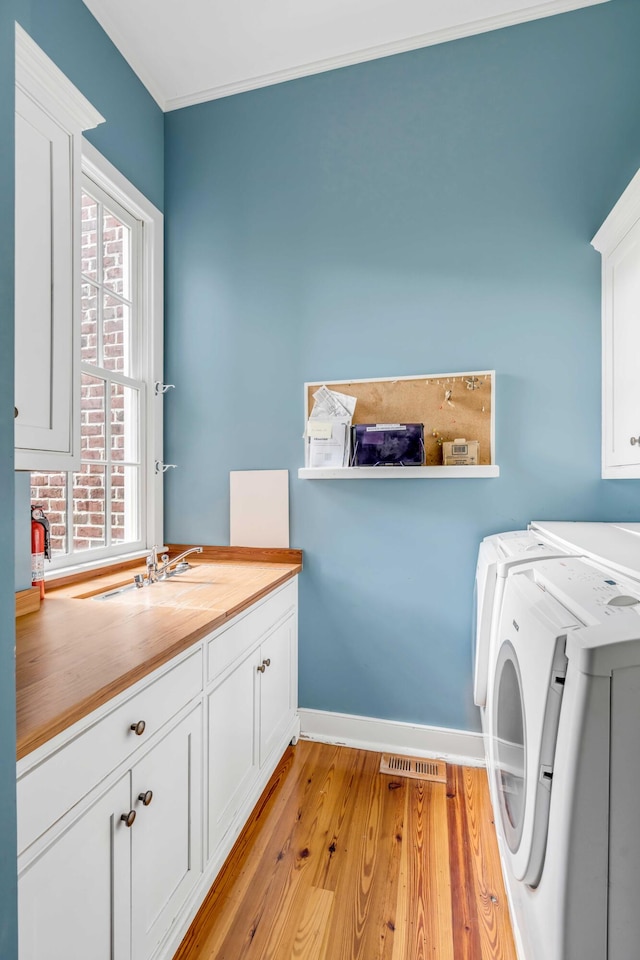 laundry area featuring crown molding, washer and clothes dryer, cabinets, sink, and light hardwood / wood-style floors