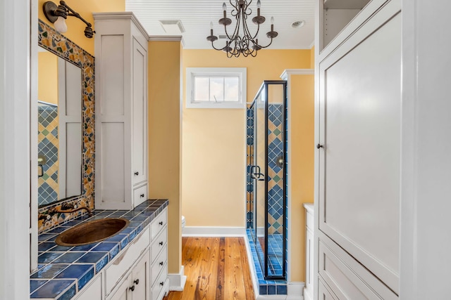 bathroom with wood-type flooring, toilet, a notable chandelier, an enclosed shower, and vanity