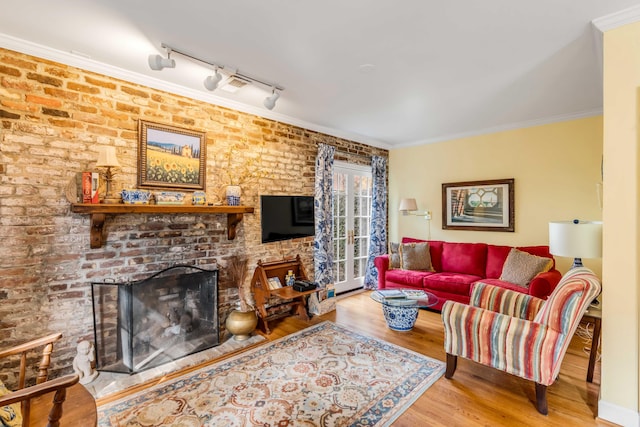 living room featuring track lighting, hardwood / wood-style flooring, ornamental molding, a fireplace, and brick wall