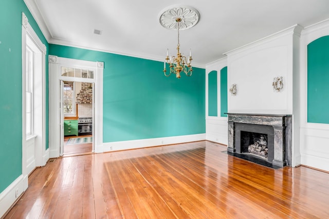 unfurnished living room featuring a fireplace, wood-type flooring, a notable chandelier, and crown molding