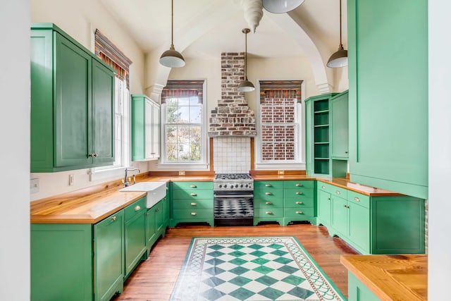 kitchen with wooden counters, green cabinets, stainless steel stove, light wood-type flooring, and decorative light fixtures