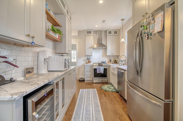 kitchen with wine cooler, decorative light fixtures, appliances with stainless steel finishes, light stone countertops, and wall chimney range hood