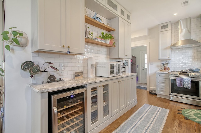 kitchen with white cabinetry, stainless steel gas range oven, wall chimney range hood, and wine cooler