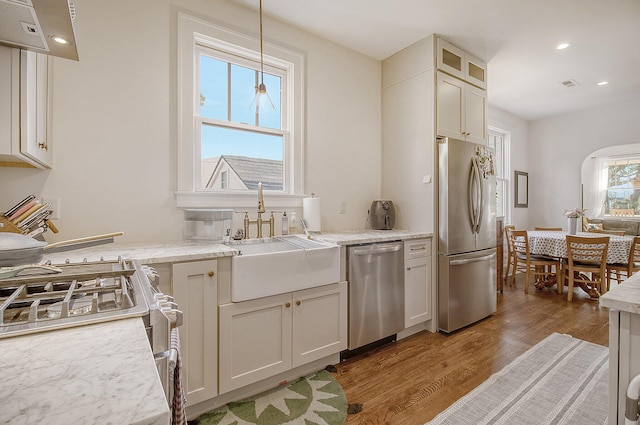 kitchen featuring appliances with stainless steel finishes, pendant lighting, white cabinetry, sink, and light wood-type flooring