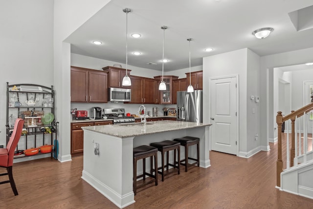 kitchen with dark wood-style flooring, a kitchen bar, pendant lighting, a center island with sink, and stainless steel appliances