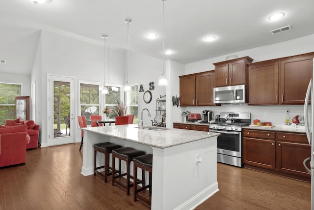 kitchen featuring appliances with stainless steel finishes, a sink, a kitchen island with sink, a kitchen breakfast bar, and high vaulted ceiling