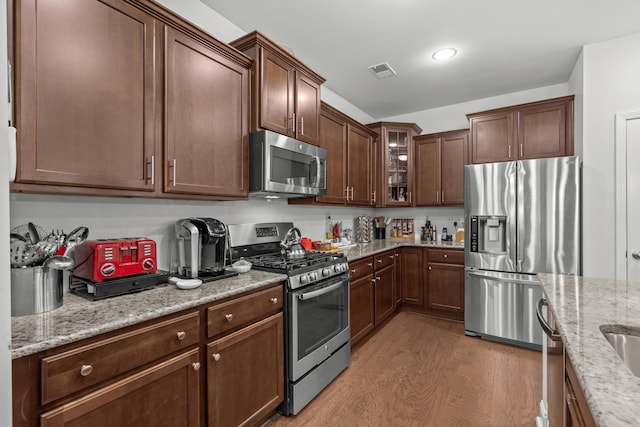 kitchen with light wood-style floors, appliances with stainless steel finishes, light stone counters, and visible vents