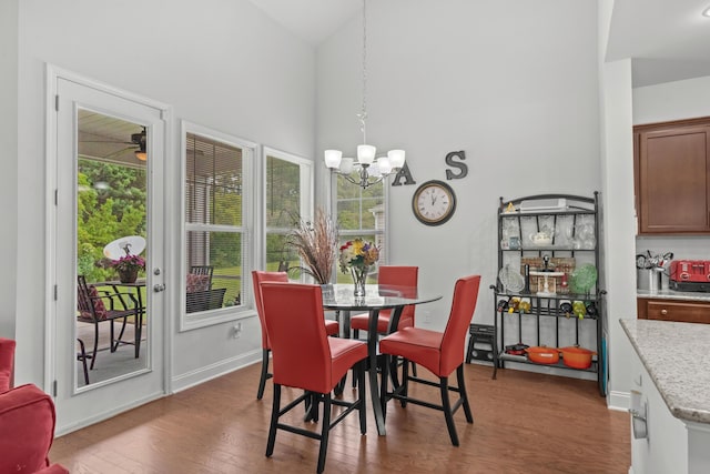 dining space with a healthy amount of sunlight, high vaulted ceiling, an inviting chandelier, and wood finished floors