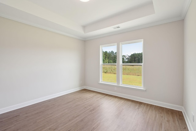 spare room featuring a tray ceiling, visible vents, baseboards, and wood finished floors