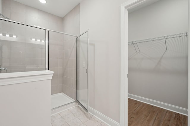 full bath featuring a walk in closet, a shower stall, baseboards, and tile patterned floors