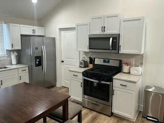 kitchen featuring light hardwood / wood-style flooring, appliances with stainless steel finishes, tasteful backsplash, white cabinets, and vaulted ceiling