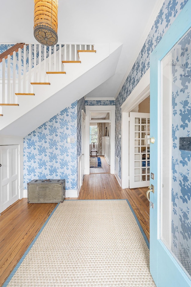 hallway with wood finished floors, baseboards, stairway, wallpapered walls, and crown molding