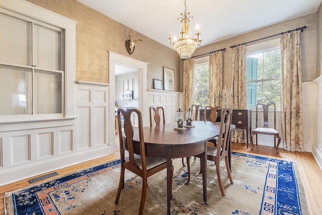 dining space with light wood finished floors, visible vents, a decorative wall, an inviting chandelier, and wainscoting