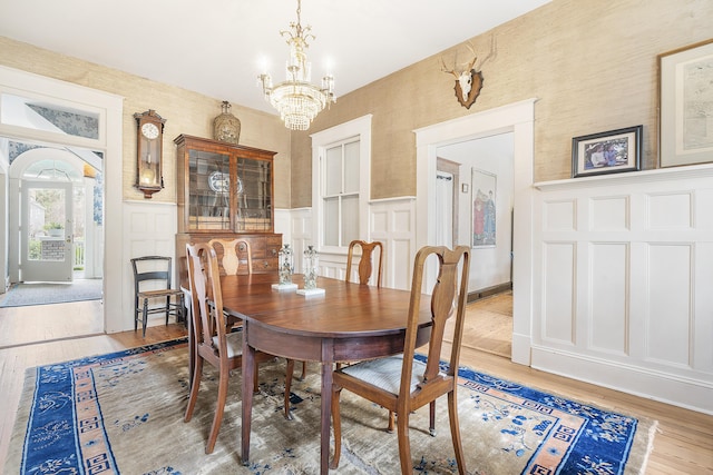 dining room with a wainscoted wall, a notable chandelier, a decorative wall, and light wood finished floors