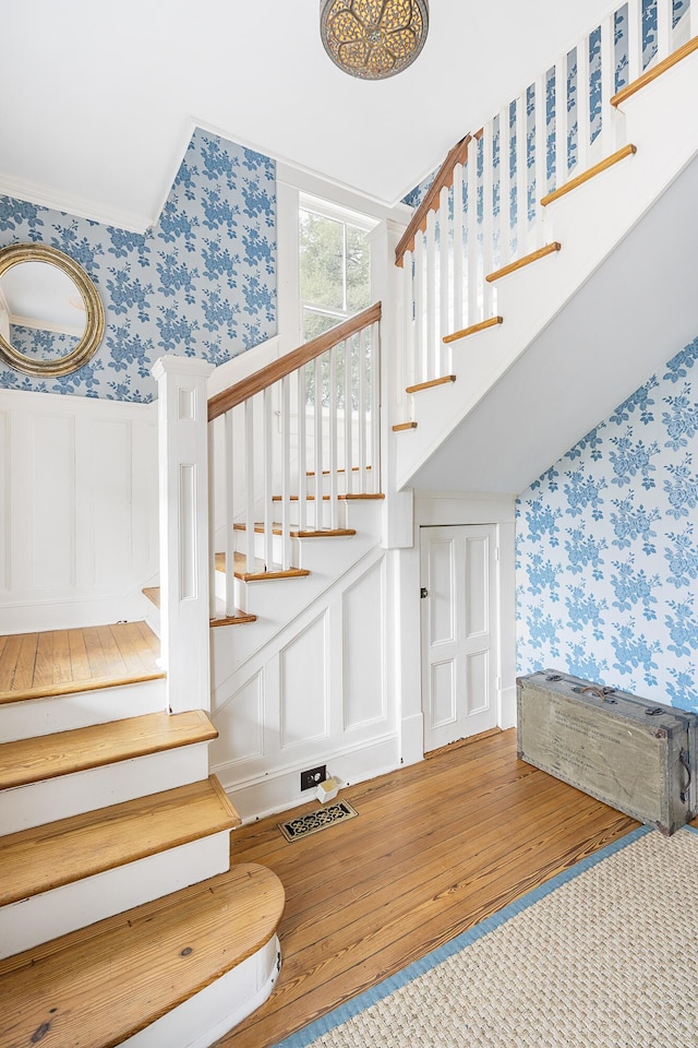 stairs with wainscoting, a decorative wall, and wallpapered walls