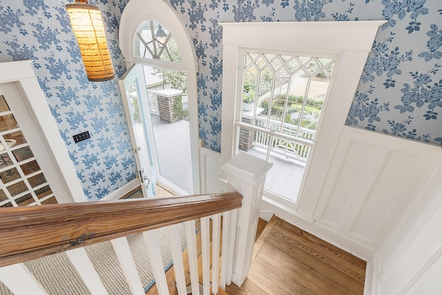 interior space featuring wallpapered walls, a decorative wall, a wainscoted wall, and wood finished floors