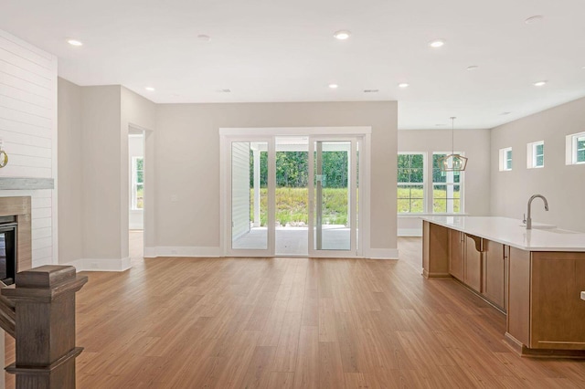 kitchen featuring pendant lighting, sink, light hardwood / wood-style flooring, a large fireplace, and an island with sink