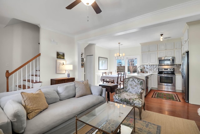 living area with crown molding, stairs, wood finished floors, and ceiling fan with notable chandelier