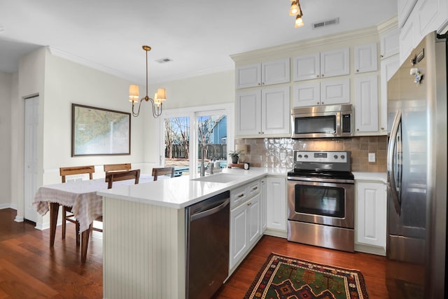 kitchen with appliances with stainless steel finishes, light countertops, a sink, and a peninsula