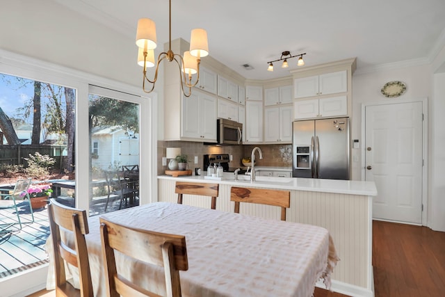 kitchen with a peninsula, light countertops, appliances with stainless steel finishes, backsplash, and crown molding