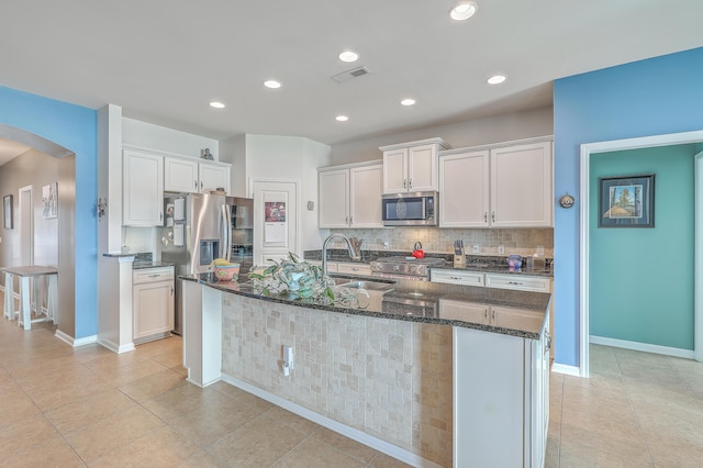 kitchen with sink, stainless steel appliances, tasteful backsplash, an island with sink, and white cabinets