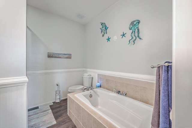 bathroom with toilet, tiled tub, and hardwood / wood-style flooring