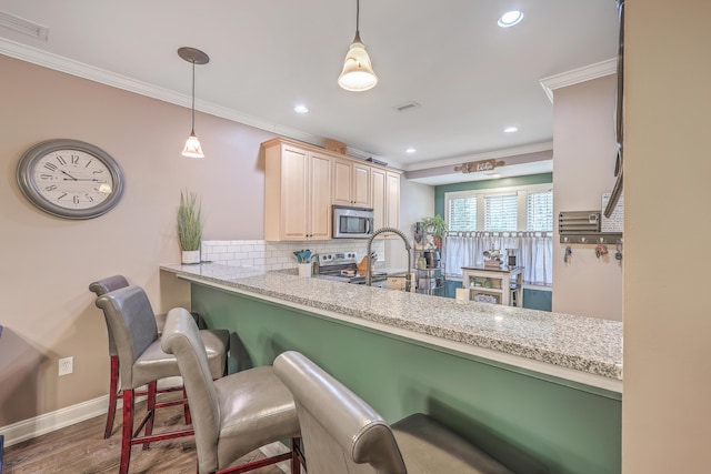 kitchen featuring a breakfast bar area, appliances with stainless steel finishes, kitchen peninsula, ornamental molding, and decorative light fixtures