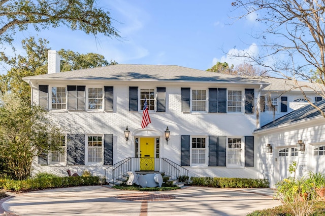 view of front of house featuring brick siding, driveway, and a chimney