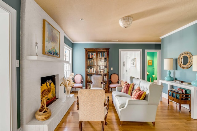 living room with a fireplace with raised hearth, ornamental molding, light wood-type flooring, and baseboards