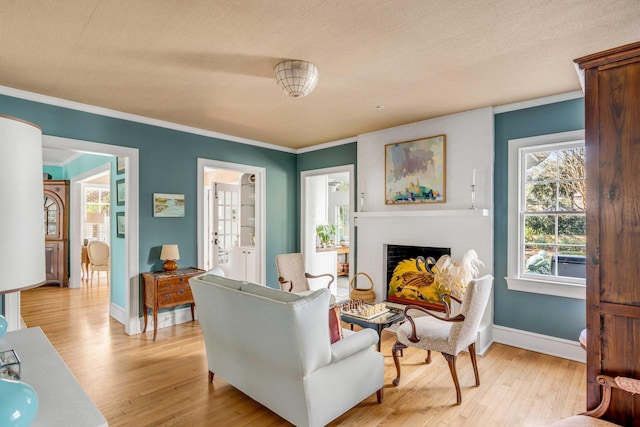 sitting room featuring a textured ceiling, a fireplace, baseboards, light wood finished floors, and crown molding