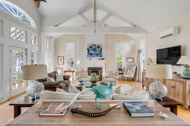 living room featuring high vaulted ceiling, a glass covered fireplace, a wall unit AC, and light wood finished floors