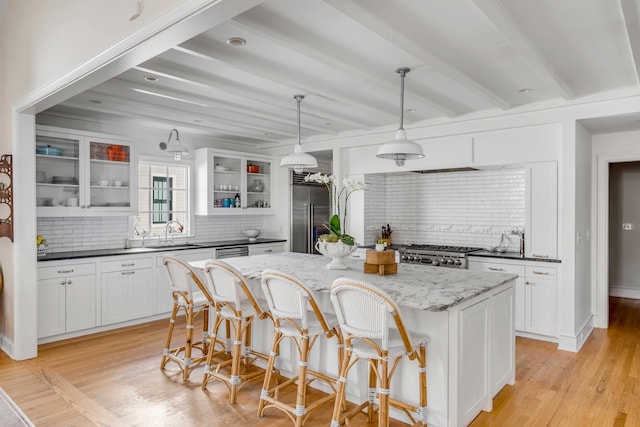 kitchen featuring decorative light fixtures, appliances with stainless steel finishes, glass insert cabinets, white cabinetry, and a kitchen island