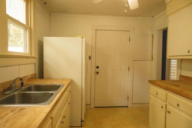 kitchen with sink, ceiling fan, ornamental molding, butcher block countertops, and white cabinetry