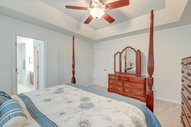 carpeted bedroom featuring ensuite bath, ceiling fan, and a tray ceiling