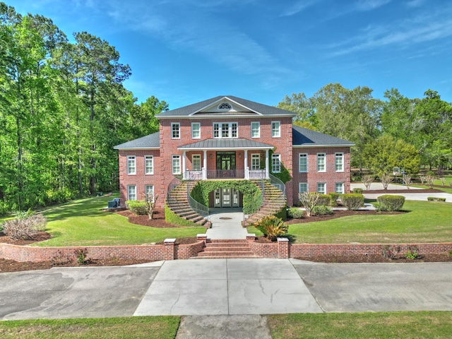 view of front of property with covered porch, stairs, brick siding, a front lawn, and a standing seam roof