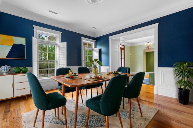 dining space featuring visible vents, an inviting chandelier, ornamental molding, light wood-type flooring, and wainscoting