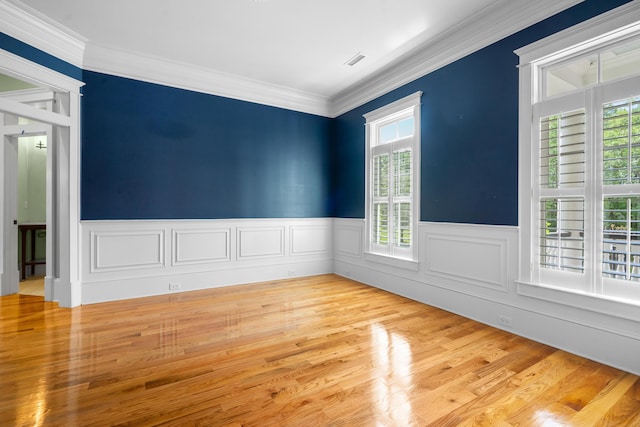 spare room featuring crown molding, wood finished floors, wainscoting, and visible vents
