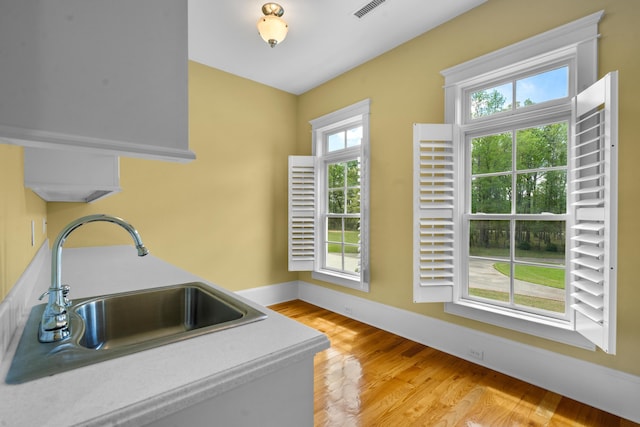 kitchen with light wood finished floors, visible vents, baseboards, and a sink
