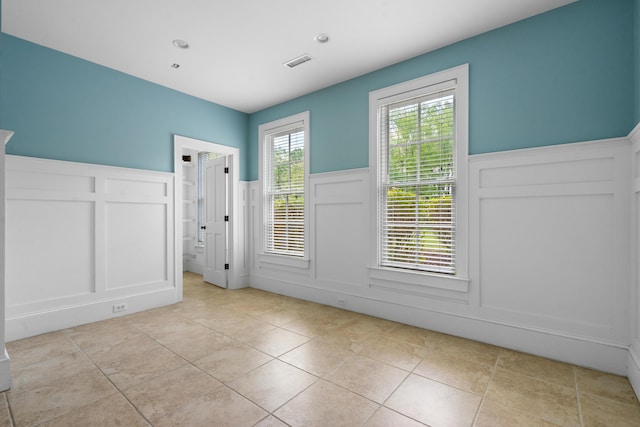 interior space with a decorative wall, light tile patterned floors, wainscoting, and visible vents