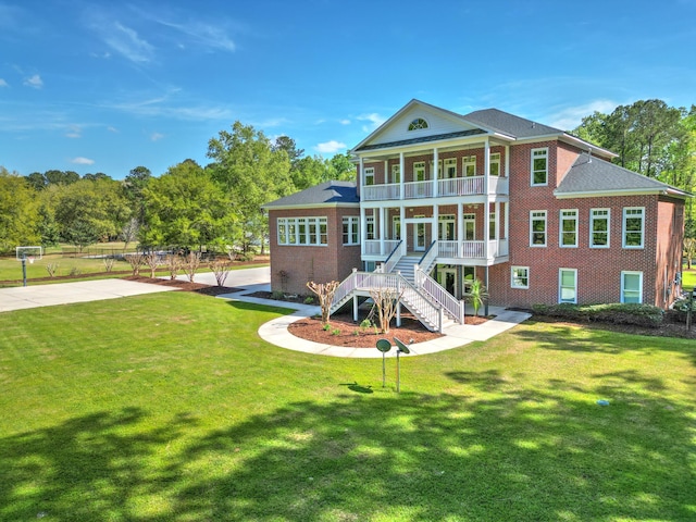 back of property with a yard, a porch, brick siding, and a balcony