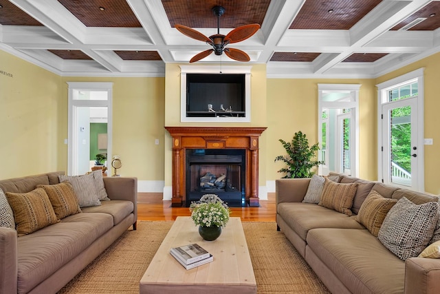 living room with ornamental molding, ceiling fan, beam ceiling, light wood finished floors, and a fireplace with flush hearth