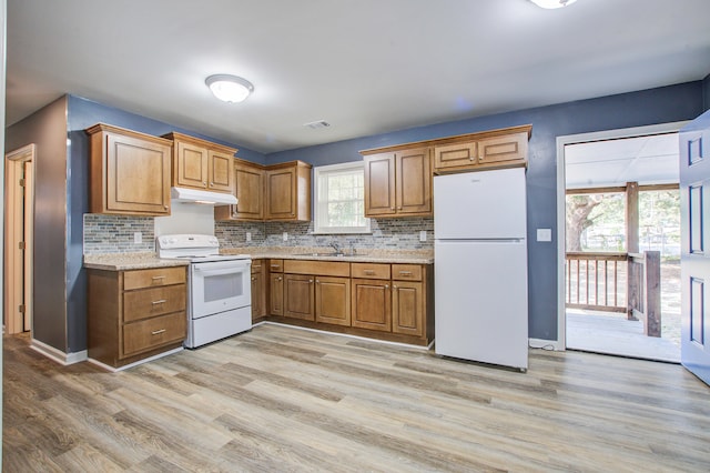 kitchen with white appliances, backsplash, sink, light hardwood / wood-style flooring, and light stone countertops