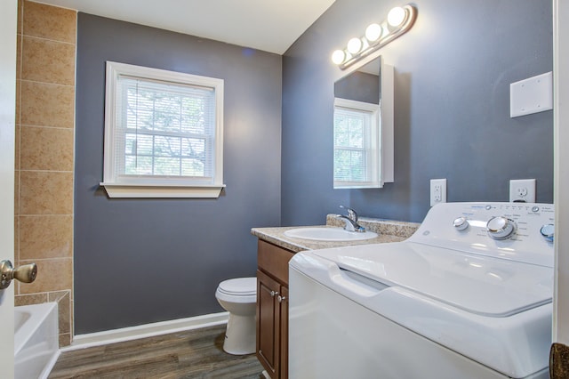 bathroom featuring vanity, a bath, hardwood / wood-style flooring, toilet, and washer / dryer