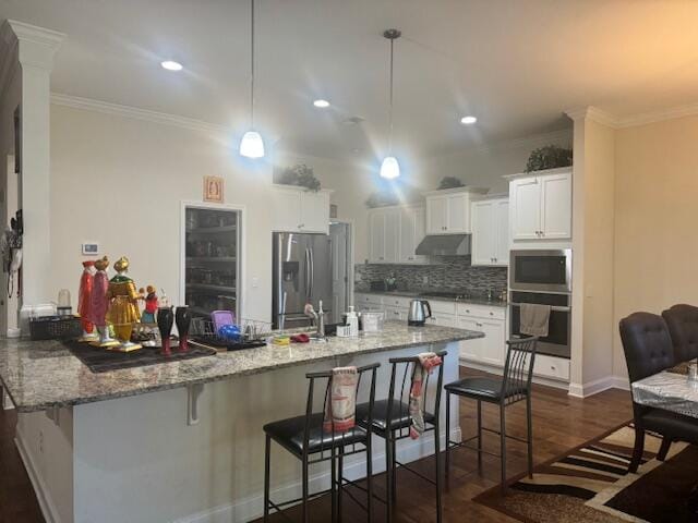 kitchen featuring pendant lighting, white cabinets, appliances with stainless steel finishes, light stone counters, and a breakfast bar area