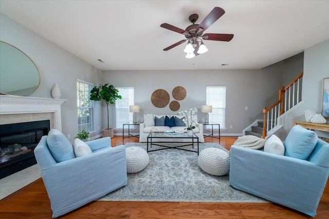 living room with a tile fireplace, wood-type flooring, and ceiling fan