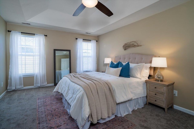 carpeted bedroom with ceiling fan and a tray ceiling