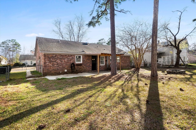 back of house featuring brick siding, fence, an outdoor fire pit, a lawn, and a patio area