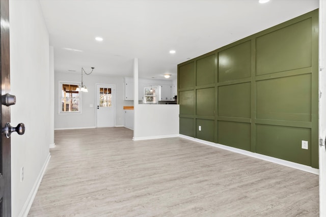 unfurnished living room with a decorative wall, recessed lighting, baseboards, and light wood-style floors