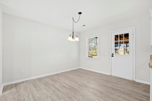 empty room with a notable chandelier, visible vents, light wood-type flooring, and baseboards