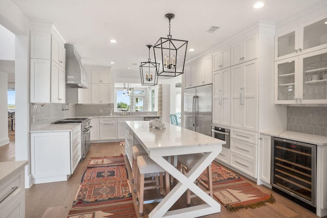 kitchen featuring white cabinets, wine cooler, tasteful backsplash, wall chimney exhaust hood, and appliances with stainless steel finishes